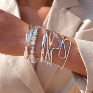 Detail of silver geometric bracelets and chain set on a beige blazer sleeve