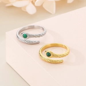 Macro detail of gold and silver snake rings with green malachite stones on a pink stand