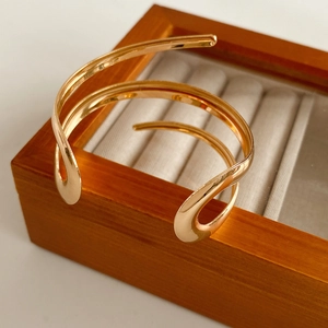 Dettaglio di un bracciale a fascia aperta dorato lucido in un portagioie di legno