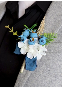 Detail of handmade groom boutonniere with blue berries and white flowers on a suit