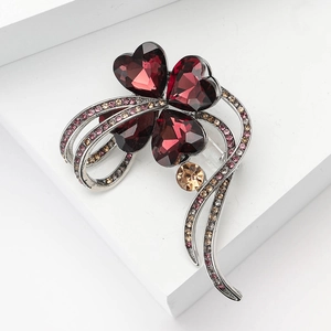 Detail of silver clover brooch featuring large red heart crystals and pink rhinestones