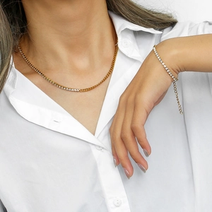Detail of gold Cuban link chain necklace and zircon bracelet set on a white shirt