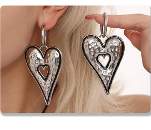 Close-up of silver textured heart earrings with hollow center and black enamel outlines