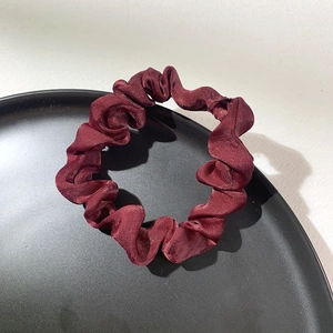 Detailed close-up of a deep red satin scrunchie placed on a black round tray