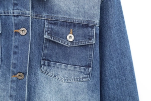 Detailed macro view of denim jacket chest pocket with metallic jeans buttons and texture