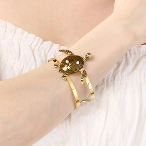 Detail view of a golden turtle bangle with green enamel and pearls on white fabric