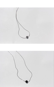 Macro detail of minimalist silver chain with a dark grey pearl pendant on white background