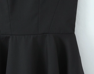 Close-up of black backless dress featuring pleated waist detail and woven fabric texture
