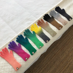Flat lay of colorful gradient knit gloves in various shades on textured fabric