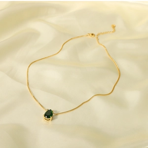Close-up of 18k gold plated drop necklace with green pear-shaped zircon on silk fabric