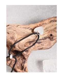 Detail view of a silver heart pendant on a black woven cord set against a rustic wood background