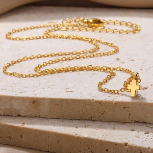 Detail view of the gold stainless steel cross pendant necklace on a natural stone surface