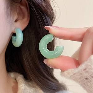 Detailed view of light green C-shaped resin earrings with marble texture on ear lobe