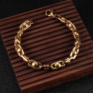 Men's gold stainless steel bracelet featuring flat rivet links on a wooden stand