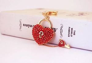Close-up of heart lock keychain with red rhinestones and gold key on white book