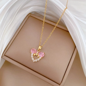 Golden bow heart necklace with pink zircon stones on white silk background