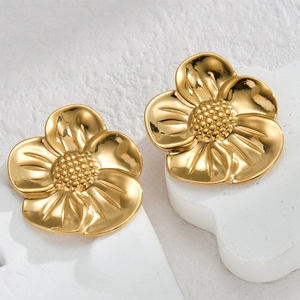 Polished 18K gold flower stud earrings with beaded center on a textured background