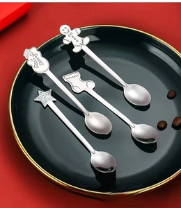 Close-up of four stainless steel Christmas spoons with festive charms in a ceramic plate