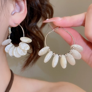 Detailed view of silver hoop earrings featuring white resin beads and oval shell pendants