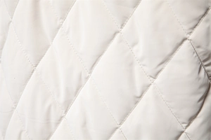 Macro detail of diamond quilted jacket fabric showing fine stitching and cream texture