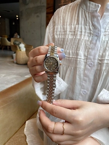 Detail of two-tone steel watch featuring a dark dial with diamond markers and calendar window