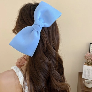 Large light blue fabric bow hair clip shown as a hair accessory in a cozy lifestyle setting