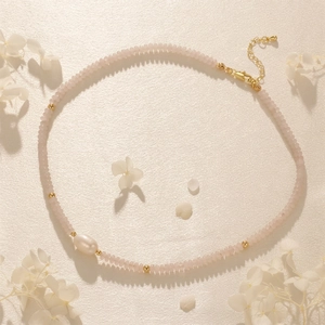 Macro shot of pink gemstone beads with a baroque pearl and golden spacers on silk fabric