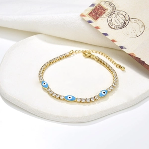 Detail of gold evil eye bracelet with white zircons and blue enamel charms on a tray