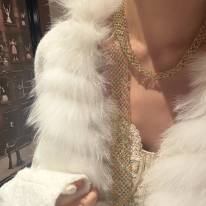 Detail of long gold mesh necklace with blue bead accents over white faux fur coat
