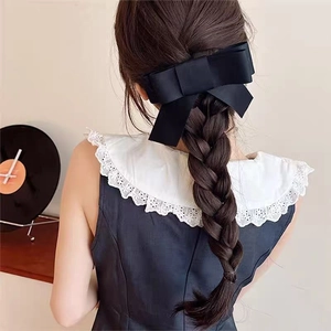 Detail of large black fabric bow hair clip styling a braided hairstyle from the back view