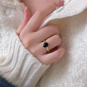 Minimalist gold ring with black oval stone worn against a cozy white sweater detail
