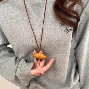 Detailed close-up of a smiling croissant pendant necklace on a brown cord with star beads