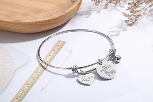 Detail of silver heart and round charms with Love and mi mama engravings on a steel bangle