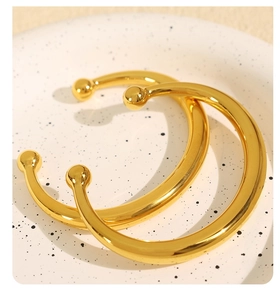 Detailed close-up of a pair of gold polished stainless steel open cuffs with ball ends