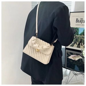 Detail of cream crossbody bag with ruffle handle and golden heart lock on black blazer