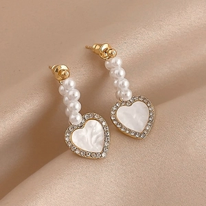 Macro view of heart earrings with pearls and rhinestones on elegant silk background