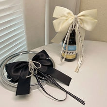Detail of satin bow hair clips with pearls and long tassel accents in black and cream