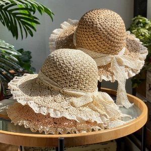 Foldable straw sun hat with delicate lace trim and ribbon bow on a wooden table