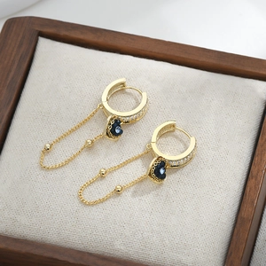 Elegant gold earrings with blue heart pendants and micro-set zircons on wooden tray