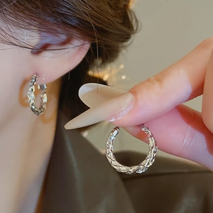 Close-up of twisted silver hoop earring featuring woven texture on a model ear