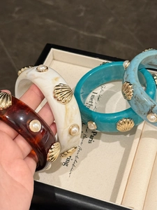 Close-up of resin cuff bracelets with gold shell accents and faux pearl details
