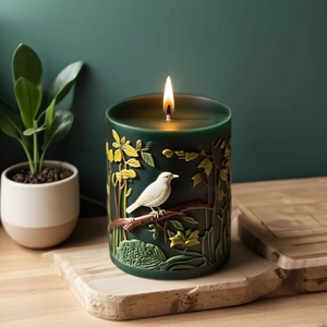 Green cylindrical candle mold with detailed bird and floral relief on wooden tray