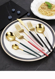 Flat lay of gold stainless steel cutlery set with colorful handles on a white ceramic plate