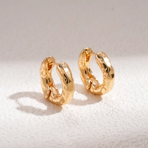 Detailed view of golden hammer-textured huggie hoop earrings with lava ripple pattern