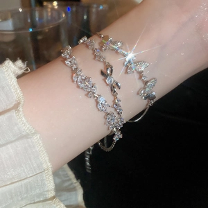 Close-up of silver-tone bracelets with zircon butterfly and leaf details on a wrist