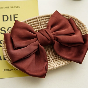 Close-up of three-layer brown satin bow hair clip on a woven tray with elegant texture