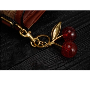 Detail of red glitter cherry charm with golden leaf on leather bag strap extension