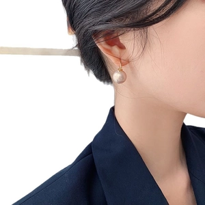 Elegant round pearl drop earrings with gold metal hooks worn by a model in a side view