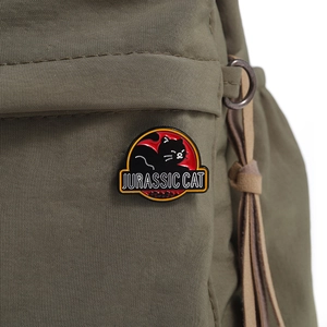 Detail of Jurassic Cat enamel pin badge on a green fabric bag with classic logo parody