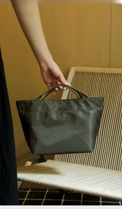 Dettaglio borsa termica in nylon verde-marrone con manici intrecciati e logo del marchio